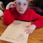 Z wizytą u świętego Mikołaja - dziewczynka przy stole pisze list do Mikołaja